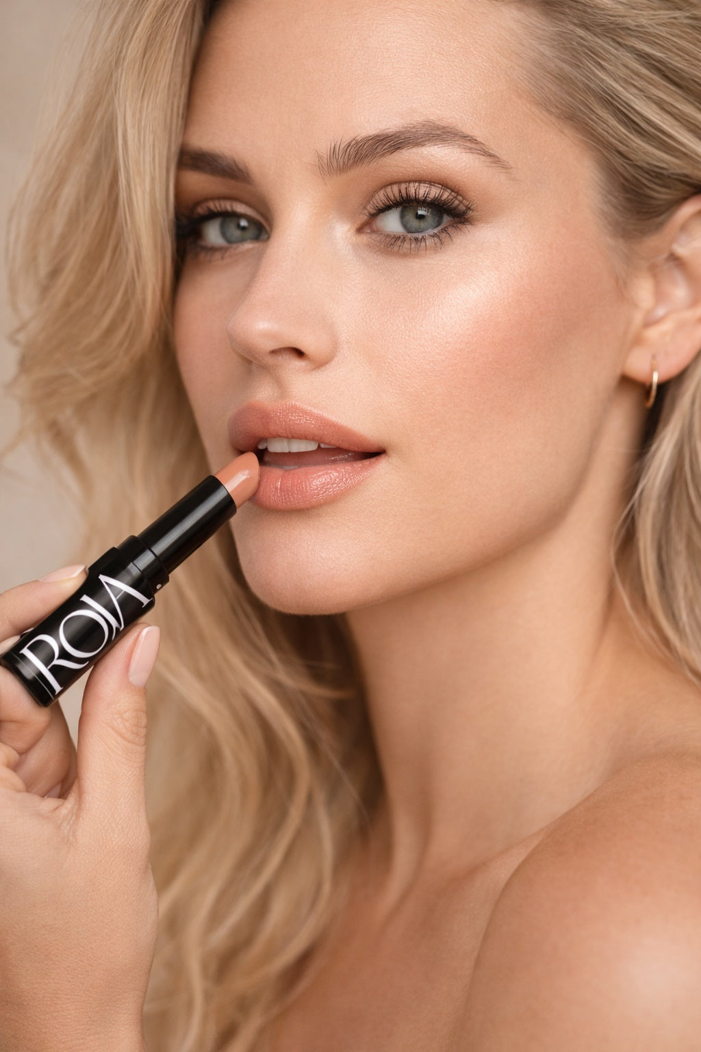 Woman applying lip Balm with a ROJA Bloom Balm product in the foreground